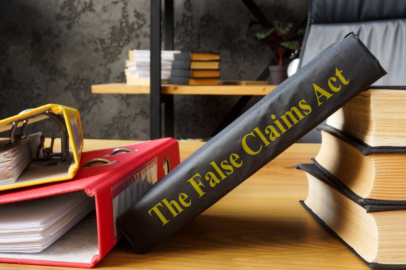 A book with a spine that reads The False Claims Act leans against a stack of books (iStock.com/designer491)