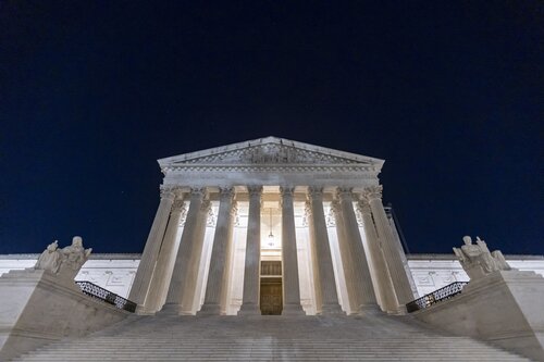 View of large white columned building at night from the bottom of the stairs
