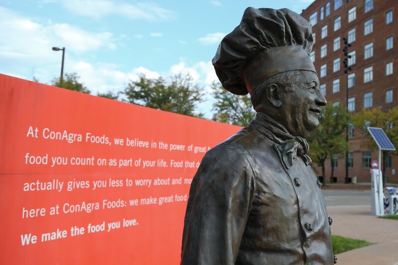 A bronze statue of a male chef wearing a hat and apron appears in an outdoor plaza