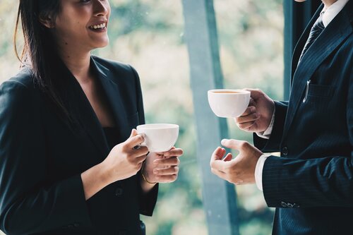 two people chatting in corporate environment holding coffee cups